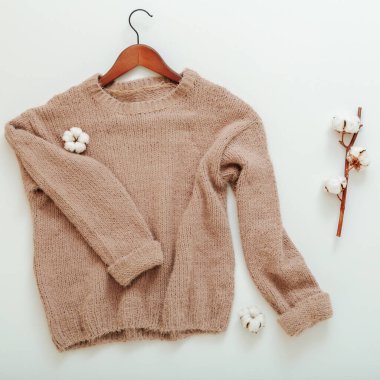 Pamuk çiçeklerle örülmüş bej süveter. Pamuk süveter düz uçar beyaz arka planda ince ince bir pamuk yatar. Sıcak, şık ev kıyafetleri, kışlık kahverengi, kalın örülü süveter. kare