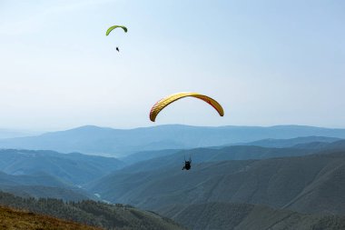 Dağlarda paraşütle atlamak. Paraşütle dağların üzerinden uçma özgürlüğü. Mavi gökyüzünün ardında Paragliding Carpathian Dağları tepeleri manzara. Aktif turizm sporu İnsanlar paraşütle uçar.