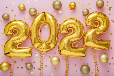 2022 yılındaki altın balonlar, pembe arka planda konfeti Noel konfeti dekoru olan kurdeleler üzerine yazı yazıyorlar. Yeni yılın kutlu olsun 2022 mektup kutlaması.