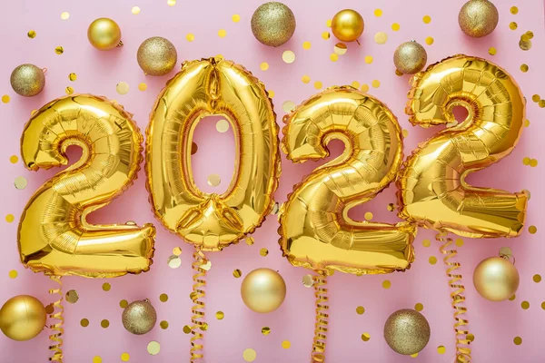 2022 year gold balloons text on ribbons with confetti Christmas gold confetti decor on pink color background. Happy New year 2022 lettering eve celebration