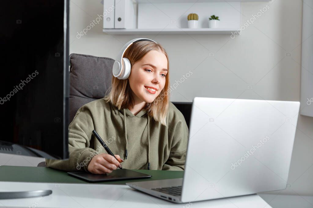 Young artist graphic designer woman drawing on digital graphic tablet by Stylus pen using laptop pc monitor at home office interior. Freelance designer in headphones studying or working remotely.