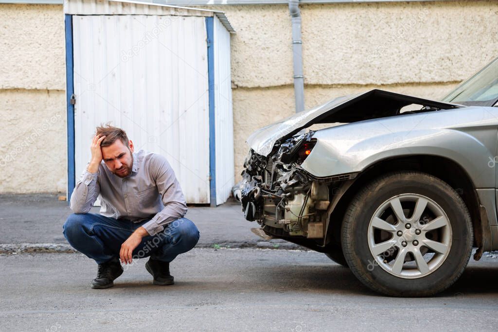 Man holding his head and suffering upset frustrated after car accident. Driver holds head near the wrecked car after car accident on the road