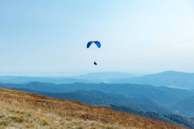 Paraşütle dağların üzerinden atlamak. Mavi gökyüzü tepelerinin ardında paraşütle atlayan manzara. Aktif turizm sporu İnsanlar paraşütle uçar.