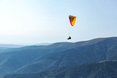 Paraşütlü adam mavi gökyüzünün arkasındaki dağların üzerinden paraşütle uçuyor. Ekstrem spor ve özgürlük