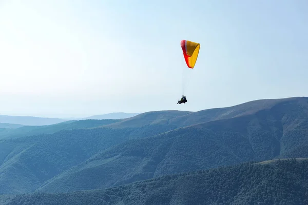 Paraşütlü adam mavi gökyüzünün arkasındaki dağların üzerinden paraşütle uçuyor. Ekstrem spor ve özgürlük — Stok fotoğraf