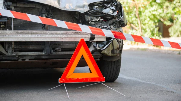 Destroyed car in car crash traffic accident on city road. Smashed broken car in accident. Red emergency stop triangle sign and Red warning police tape afore. Long web banner