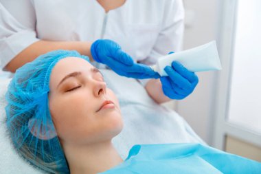 Güzellik uzmanı kadın müşteri için güzellik prosedürü uygular. Güzellik doktoru cildiyeciler kadın yüzüne nemlendirici krem ya da krem maskesi sürerler. Güzellik salonu ya da klinikte kozmetik spa prosedürü