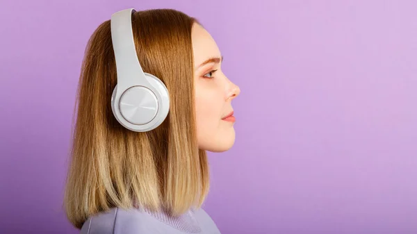 Young woman in headphones portrait looking side on copy space. Confident beautiful woman blonde hair portrait enjoy listen music in headphone isolated over purple color background. Long web banner. — Stock Photo, Image