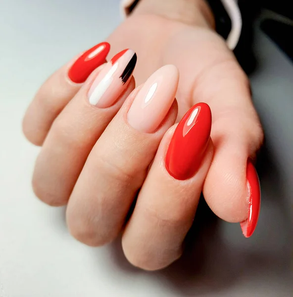 Bright red gel Polish with camouflage design and brushstrokes. A woman\'s hand with long almond-shaped nails and a multi-colored design.