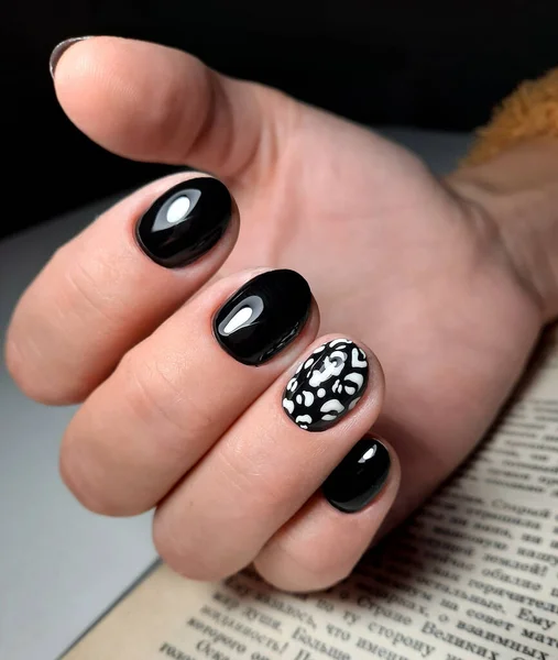 Black nails with a white leopard design on the background of the book text. Women\'s pens with black gel Polish and white geometry.