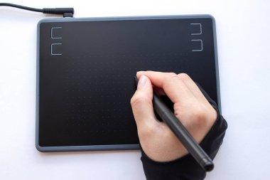 Bir insan grafik tabletine resim çizer. Çizim eldivenindeki bir el, dokunmatik bir kalem tutar. Tasarımcı ve sanatçı için kablosuz grafik tablet. Bir kadın grafik tablet üzerinde çalışıyor..