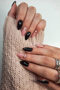 Altın desenli iki tonluk güzel bir manikür. Siyah ve kamuflaj jeli süveter giyen eller. Süslü oje kaplama.