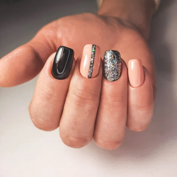 Multi-colored gel nail polish in black, beige and silver colors with a design. Professional manicure with sequins.