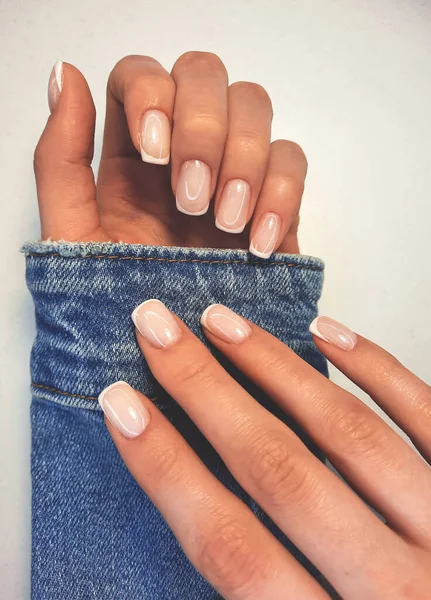 Gentle camouflage gel polish on square nails with a French design. Hands with a professional manicure in a denim jacket. Trendy nail coating with French design.