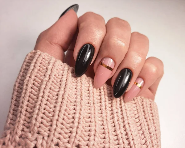 Beautiful two-tone manicure with gold design. Hands in a sweater with black and camouflage gel polish. Stylish nail polish coating.