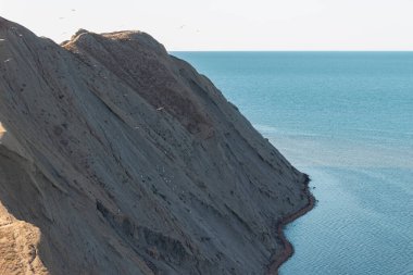Deniz kıyısında dik bir uçurum. Açık gökyüzü ve okyanusun arka planında dik bir dağ..