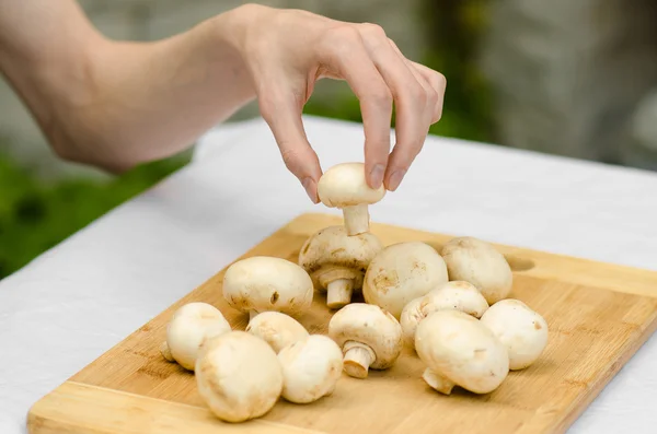 Грибы и еда: человек готовит грибы из свинины на деревянной доске на фоне зеленой травы летом — стоковое фото