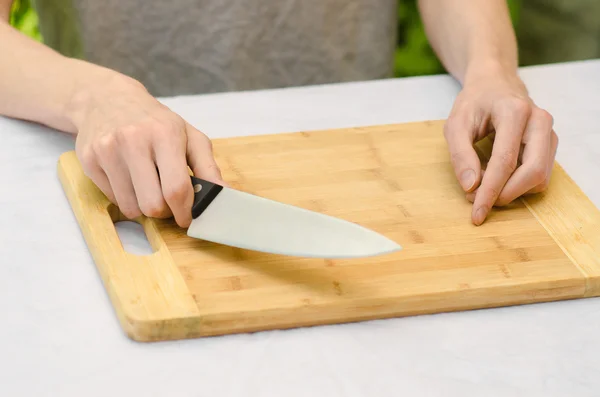 Tema della cucina: un uomo che tiene un coltello accanto a un tagliere di legno su uno sfondo di erba verde in estate — Foto Stock