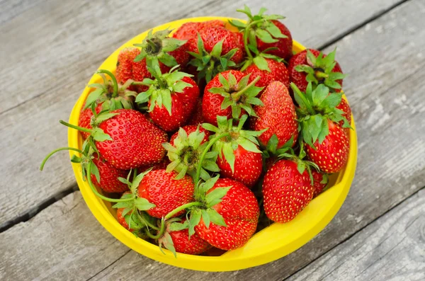 Summer berries topic: Ripe red strawberries lying in a yellow plate on a pile of gray wooden table in the garden, view from above