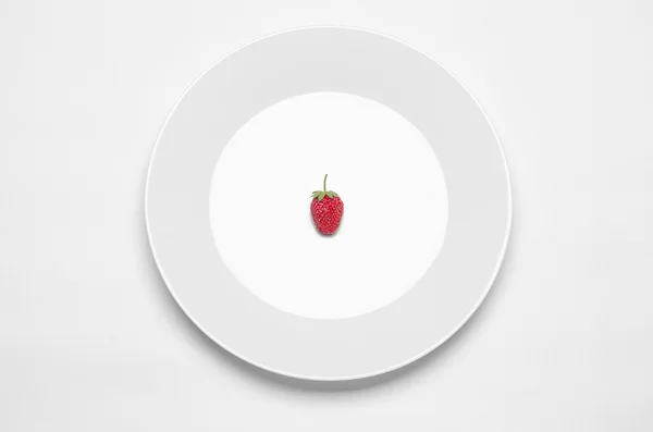 Тема: белая тарелка с клубникой, лежащей на белом столе в студии — стоковое фото