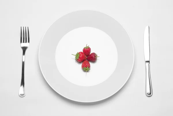 Sehat makan di restoran dan diet Topik: piring putih dengan tiga stroberi dan pisau logam dan garpu tergeletak di meja putih di studio terisolasi atas pandangan — Stok Foto