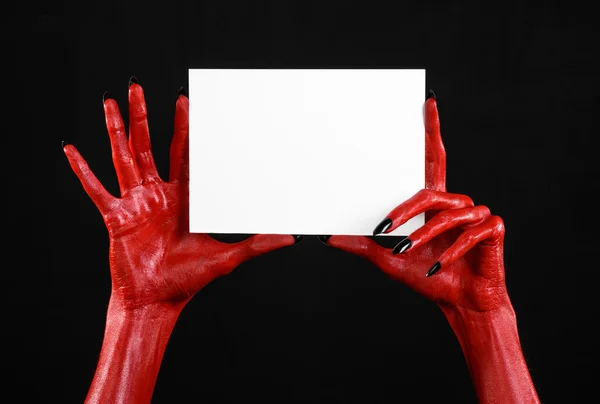 Tema de Halloween: Mão do diabo vermelho com pregos pretos segurando um cartão branco em branco em um fundo preto — Fotografia de Stock