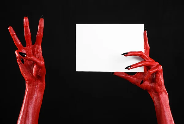 Tema de Halloween: Mão do diabo vermelho com pregos pretos segurando um cartão branco em branco em um fundo preto — Fotografia de Stock