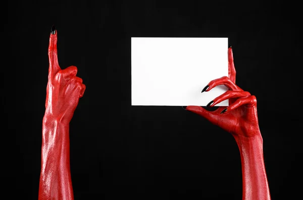 Tema di Halloween: mano del diavolo rosso con chiodi neri che tengono una carta bianca vuota su uno sfondo nero — Foto Stock