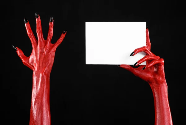 Tema de Halloween: Mão do diabo vermelho com pregos pretos segurando um cartão branco em branco em um fundo preto — Fotografia de Stock