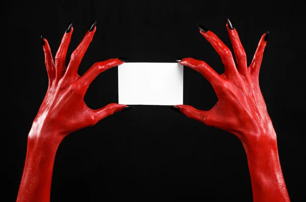 Halloween téma: Red devil ruku s černými nehty drží prázdnou bílou kartu na černém pozadí — Stock fotografie