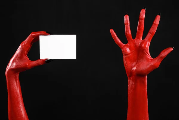 Tema de Halloween: Mão do diabo vermelho com pregos pretos segurando um cartão branco em branco em um fundo preto — Fotografia de Stock