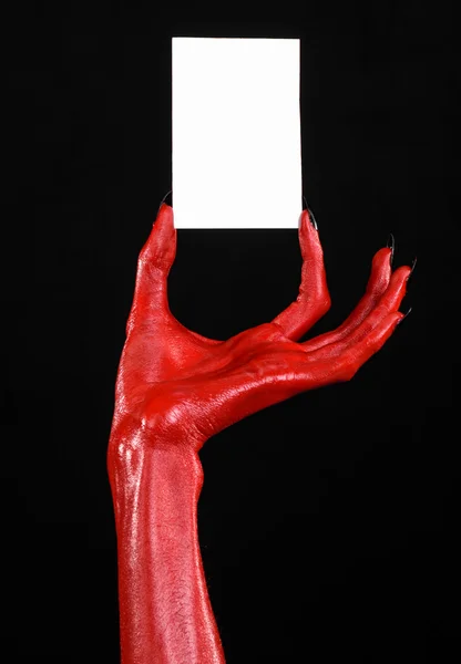 Halloweentema: Rød djevelhånd med svarte negler som holder et hvitt kort på svart bakgrunn – stockfoto