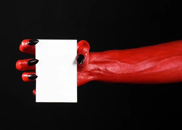 Tema de Halloween: Mão do diabo vermelho com pregos pretos segurando um cartão branco em branco em um fundo preto — Fotografia de Stock