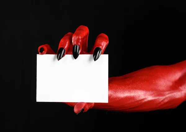 Tema de Halloween: Mão do diabo vermelho com pregos pretos segurando um cartão branco em branco em um fundo preto — Fotografia de Stock