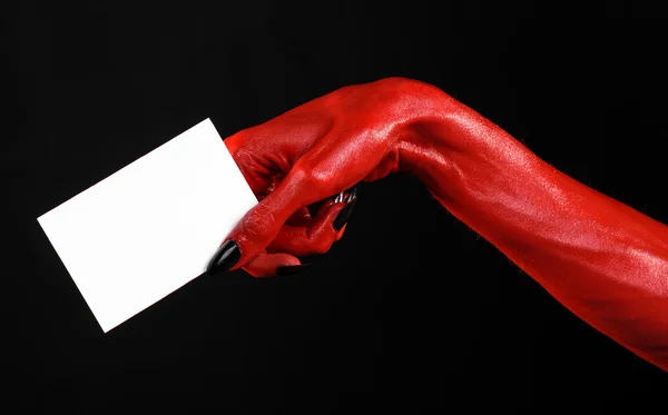 Tema de Halloween: Mão do diabo vermelho com pregos pretos segurando um cartão branco em branco em um fundo preto — Fotografia de Stock
