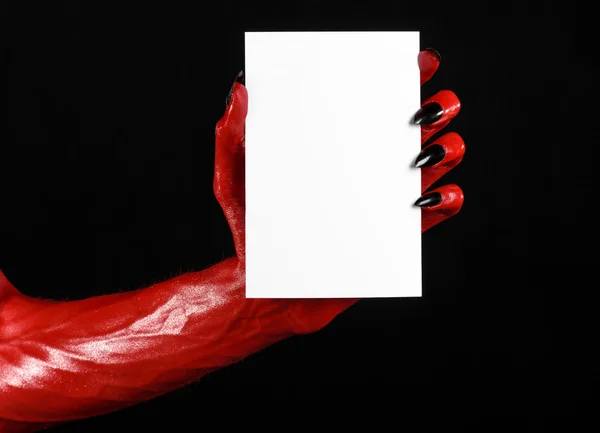 Halloweentema: Rød djevelhånd med svarte negler som holder et hvitt kort på svart bakgrunn – stockfoto