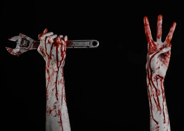 Halloween theme: bloody hand holding a big wrench on a black background — Stock Photo, Image