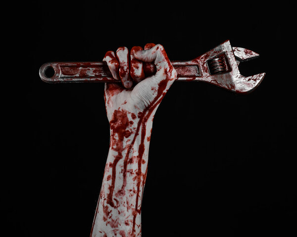 Тема Хэллоуина: окровавленная рука с большим гаечным ключом на черном фоне
