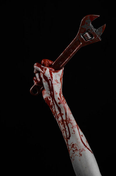 Тема Хэллоуина: окровавленная рука с большим гаечным ключом на черном фоне
