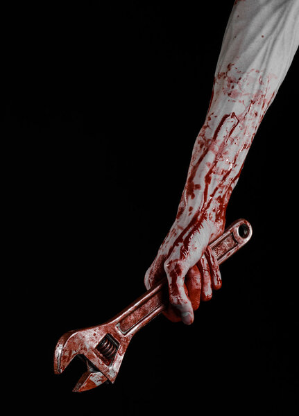 Тема Хэллоуина: окровавленная рука с большим гаечным ключом на черном фоне
