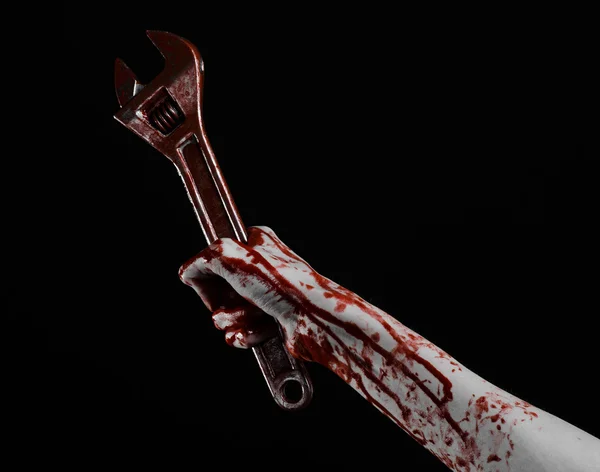 Halloween theme: bloody hand holding a big wrench on a black background — Stock Photo, Image