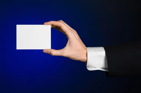 Business en reclame onderwerp: Man in zwart pak met een witte Blanco kaart in zijn hand op een donker blauwe achtergrond in studio geïsoleerd — Stockfoto