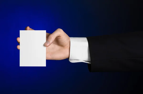 Business en reclame onderwerp: Man in zwart pak met een witte Blanco kaart in zijn hand op een donker blauwe achtergrond in studio geïsoleerd — Stockfoto