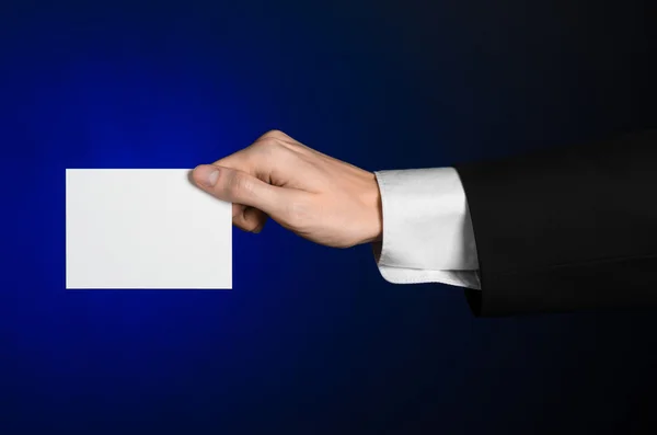 Business en reclame onderwerp: Man in zwart pak met een witte Blanco kaart in zijn hand op een donker blauwe achtergrond in studio geïsoleerd — Stockfoto