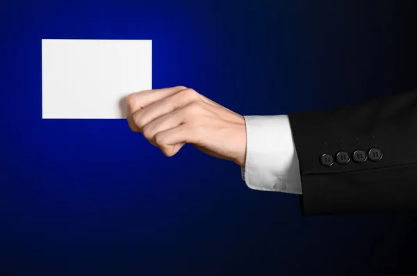 Business en reclame onderwerp: Man in zwart pak met een witte Blanco kaart in zijn hand op een donker blauwe achtergrond in studio geïsoleerd — Stockfoto