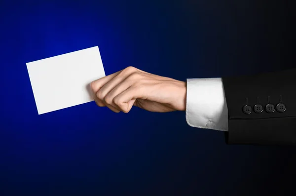 Tema comercial y publicitario: Hombre de traje negro sosteniendo una tarjeta blanca en blanco en su mano sobre un fondo azul oscuro en estudio aislado — Foto de Stock