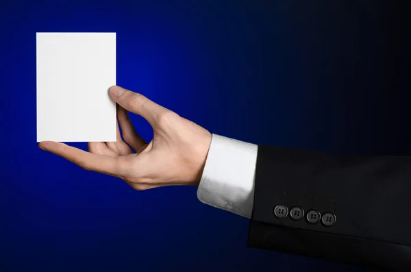 Tópico de negócios e publicidade: Homem de terno preto segurando um cartão branco na mão em um fundo azul escuro em estúdio isolado — Fotografia de Stock
