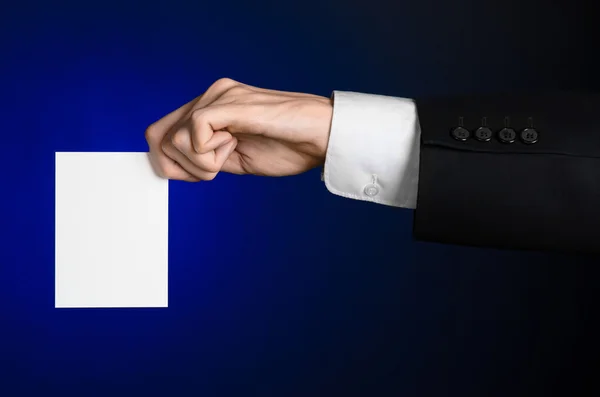 Business and advertising topic: Man in black suit holding a white blank card in his hand on a dark blue background in studio isolated — Stock Photo, Image