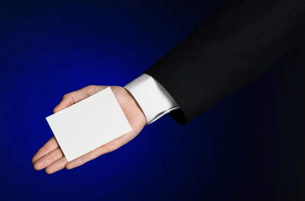 Business en reclame onderwerp: Man in zwart pak met een witte Blanco kaart in zijn hand op een donker blauwe achtergrond in studio geïsoleerd — Stockfoto