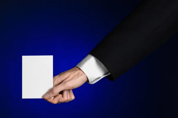 Business and advertising topic: Man in black suit holding a white blank card in his hand on a dark blue background in studio isolated — Stock Photo, Image